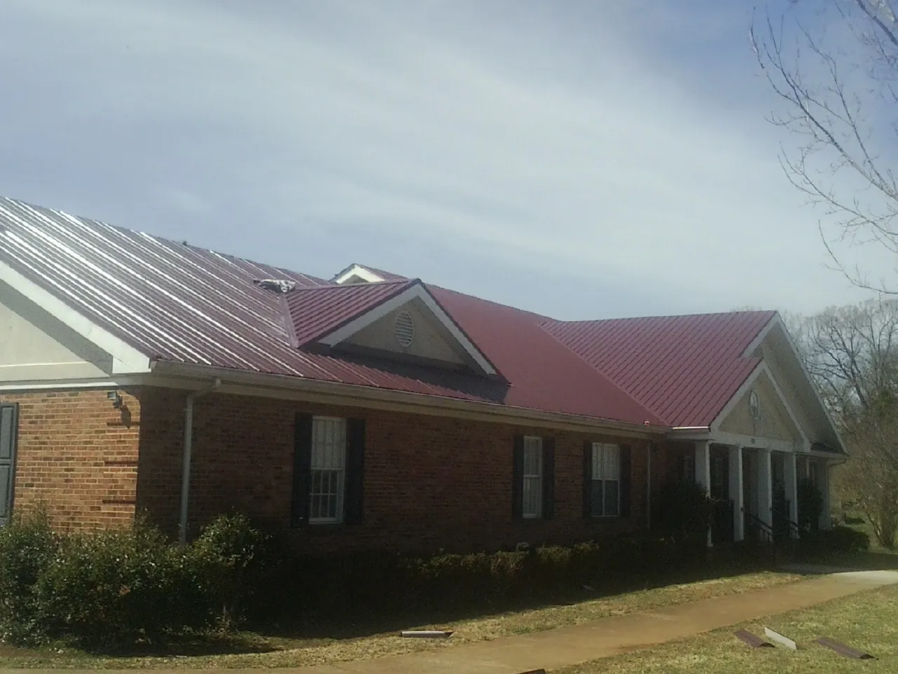 Red metal roof with gabled entries on a long brick building, from a Hail Damage Roof Repair job in Tualatin