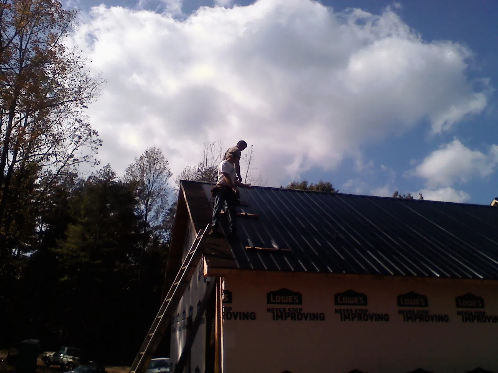 Roofer fastening dark metal panels high against a cloudy sky in Tualatin