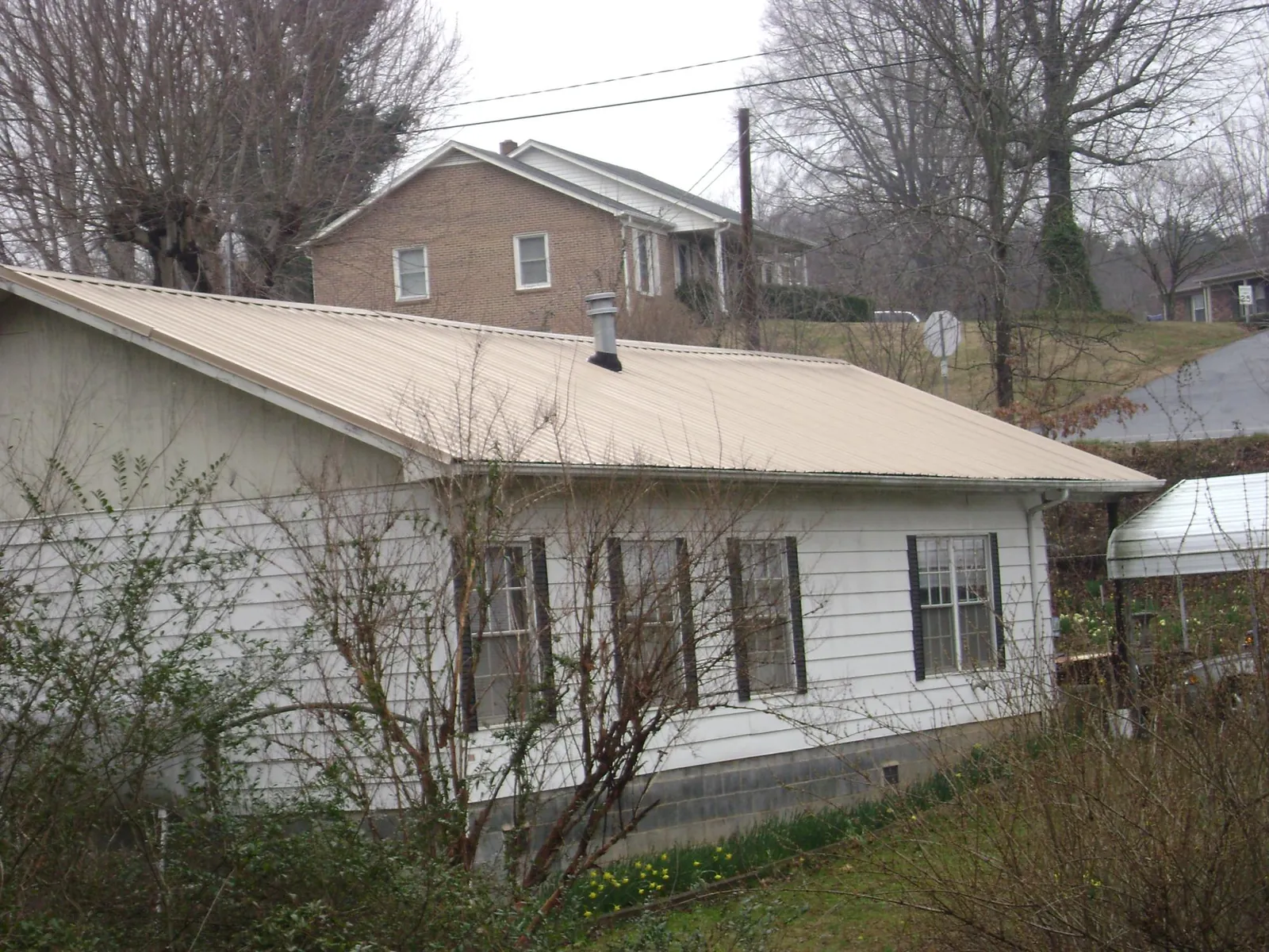 Tan metal roof on a white sided house set into a hillside — Commercial Roofing by Roofing Brothers in Tualatin